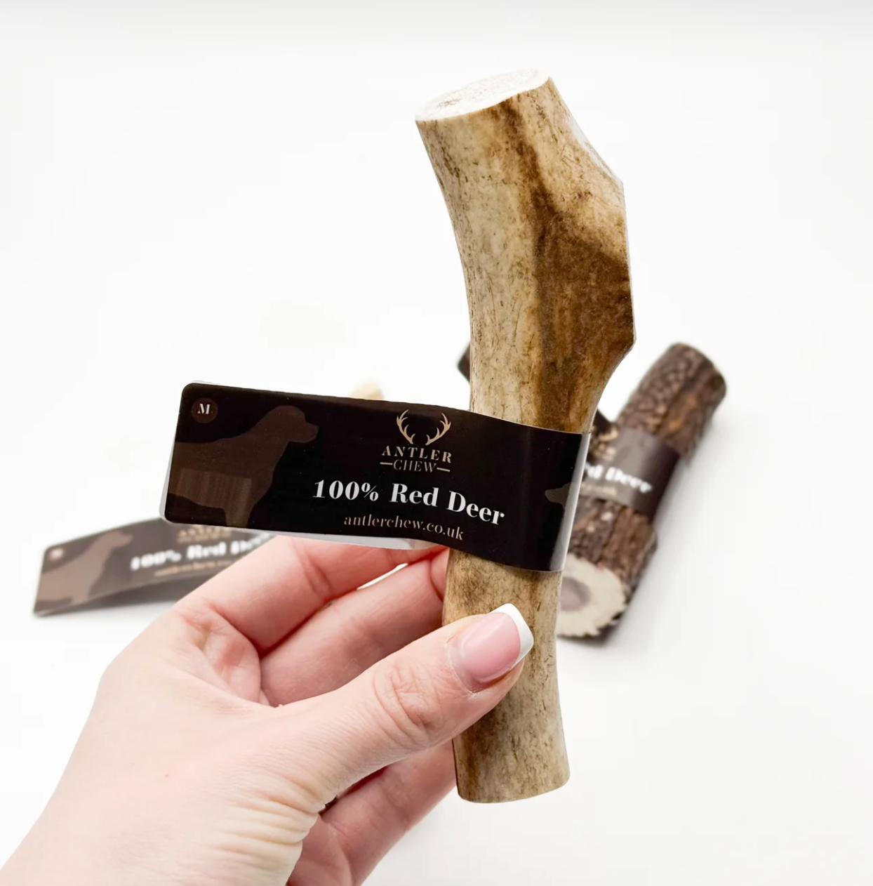 Hand holding a red deer antler chew with a label on a white background