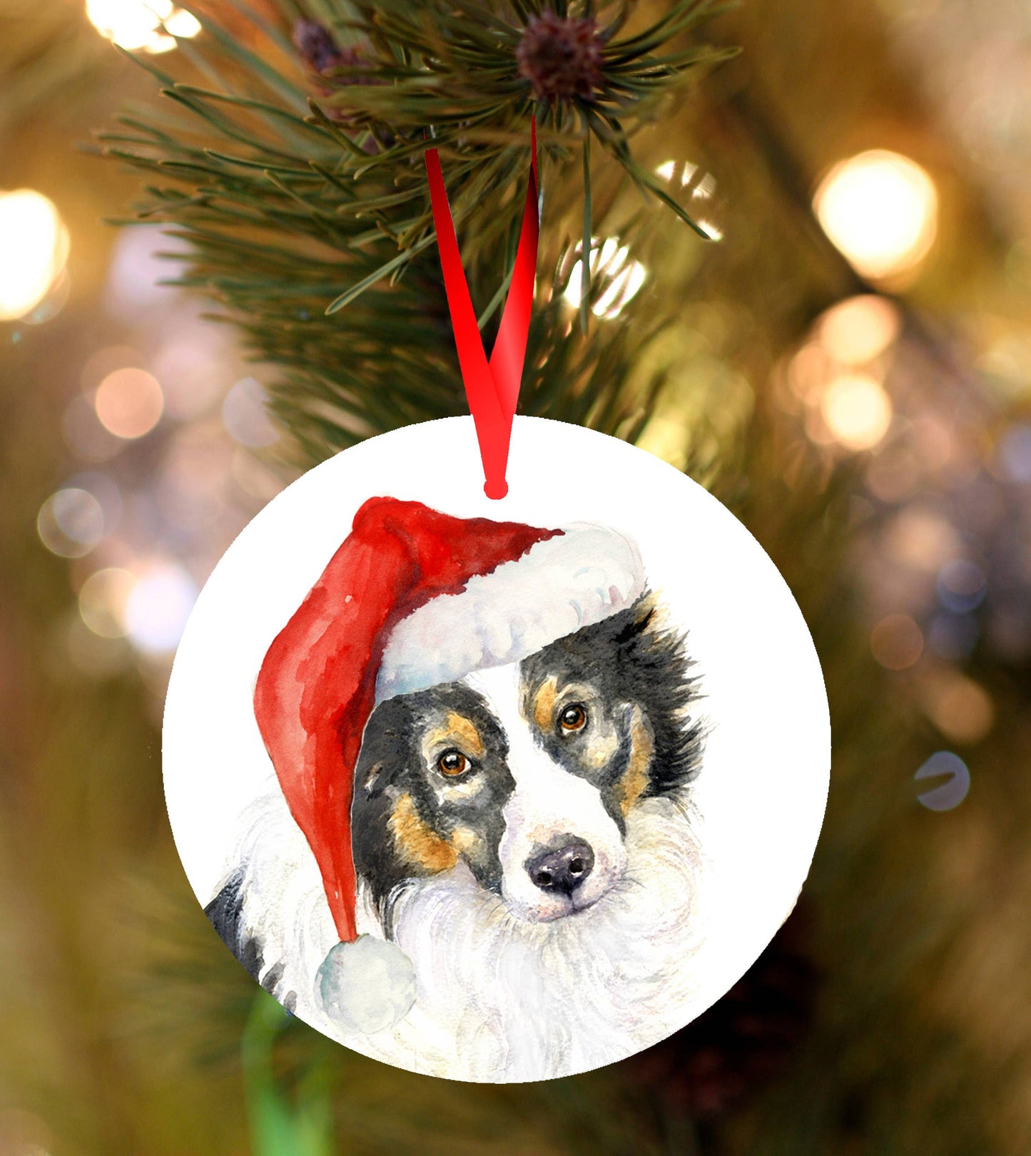 Ceramic Christmas ornament featuring a festive watercolour Border Collie wearing a Santa hat, hanging from a red ribbon on a Christmas tree with warm golden bokeh lights