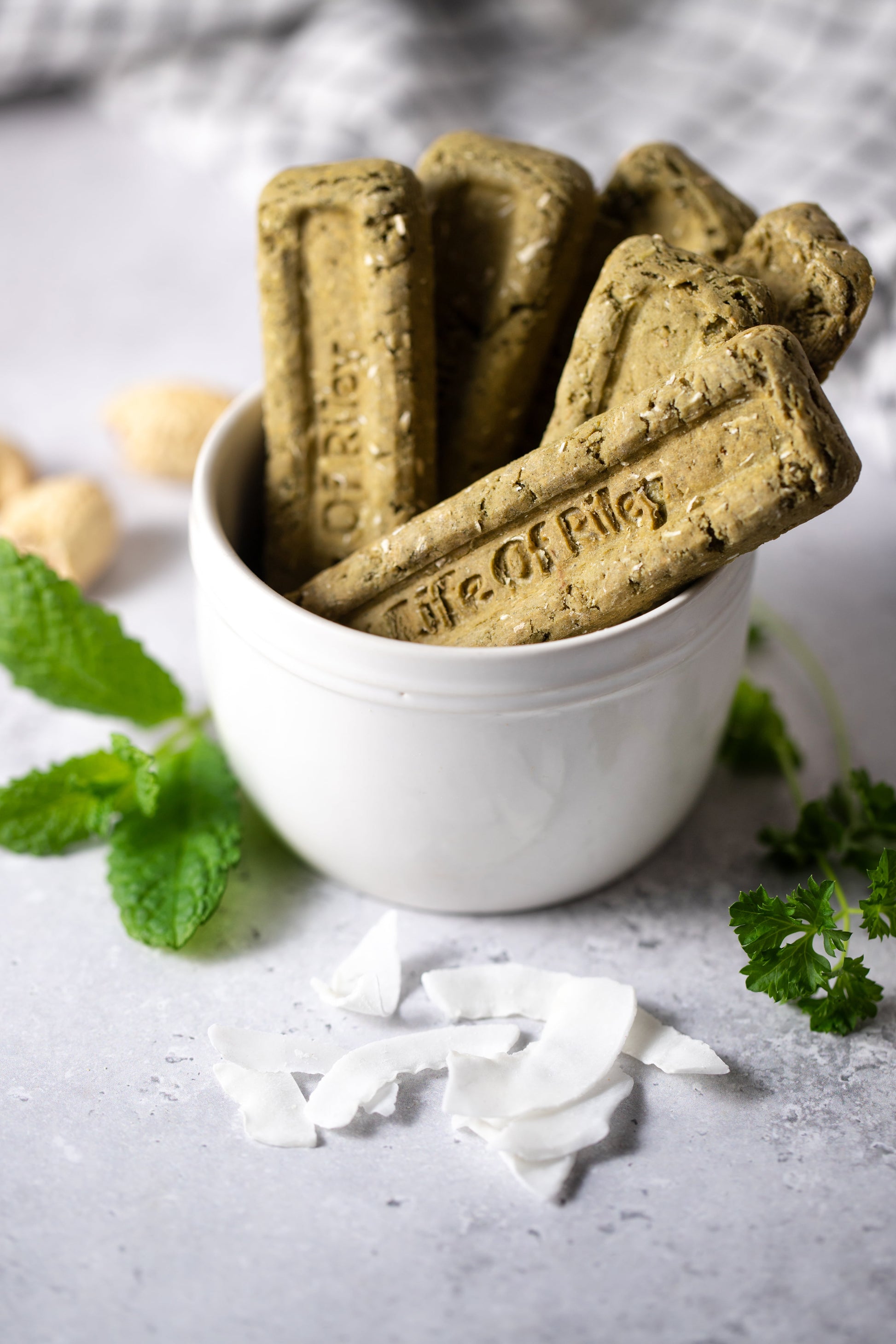 Life of Riley Minty Dental Sticks in a white bowl with fresh herbs on a grey surface — natural grain-free oral care treats for dogs