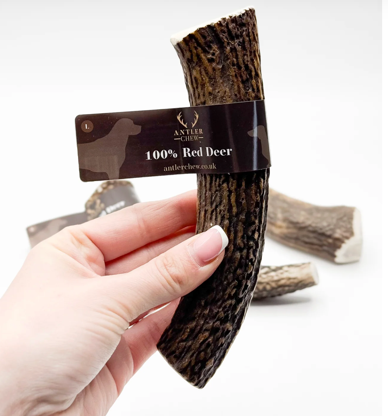Hand holding a red deer antler chew with a label, set against a white background.
