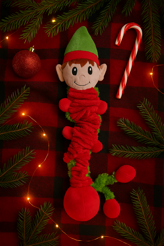Flat-lay of Bungee Elf Christmas Dog Toy on red plaid blanket with fairy lights, candy cane, bauble, and pine branches