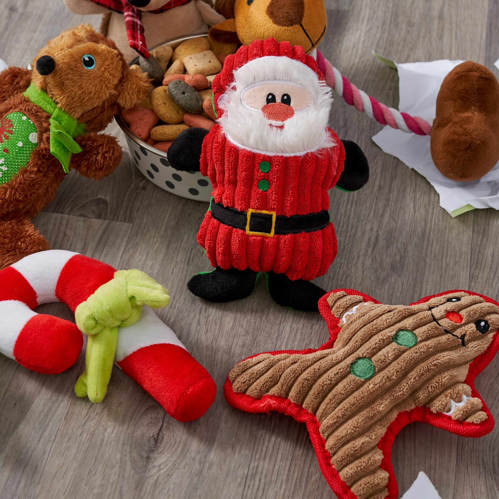 Flat-lay of assorted Christmas plush dog toys beside a bowl of treats